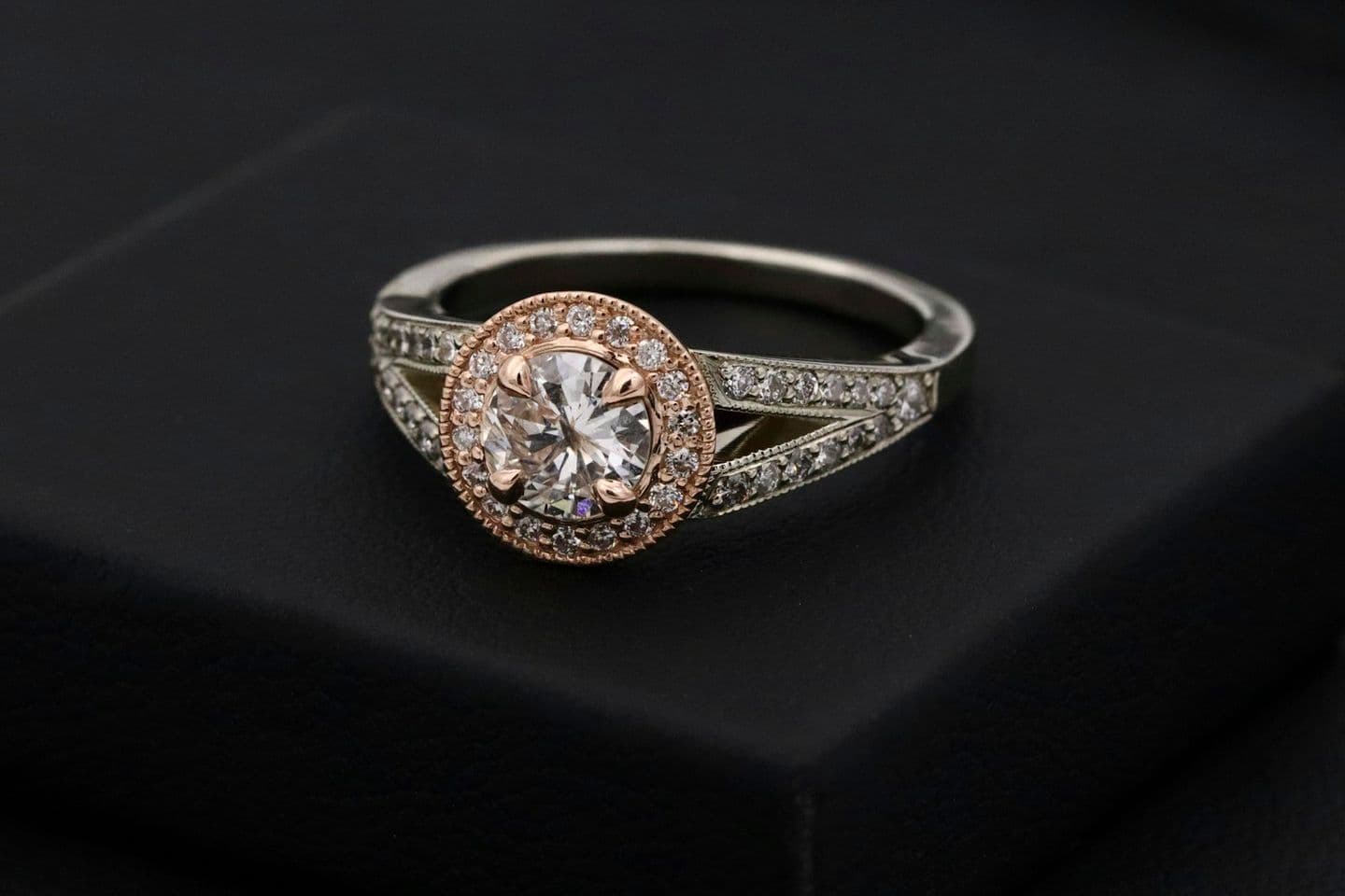 A diamond ring with a rose-gold halo on a black box