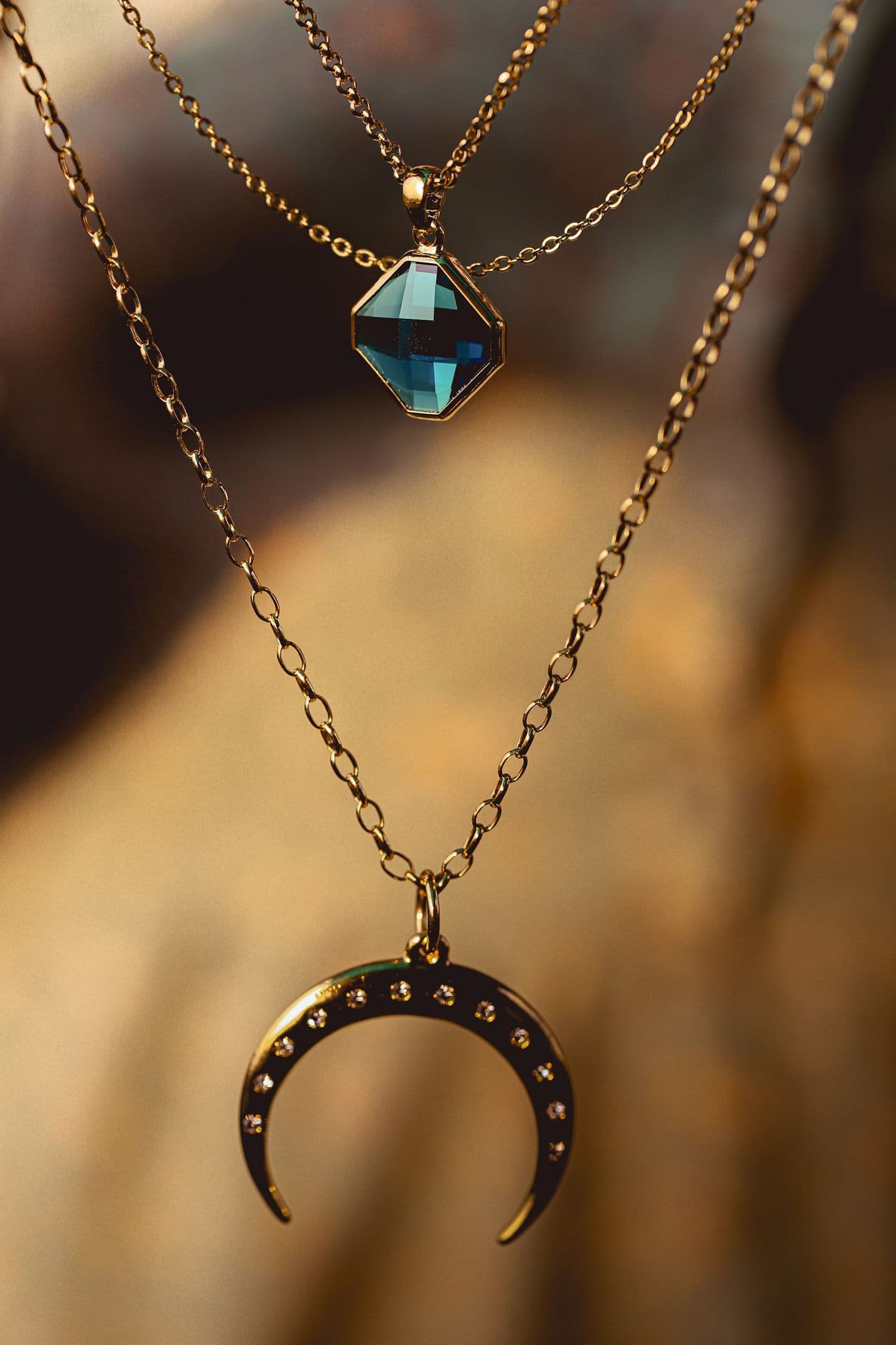 Two layered gold necklaces with a blue stone and a crescent pendant